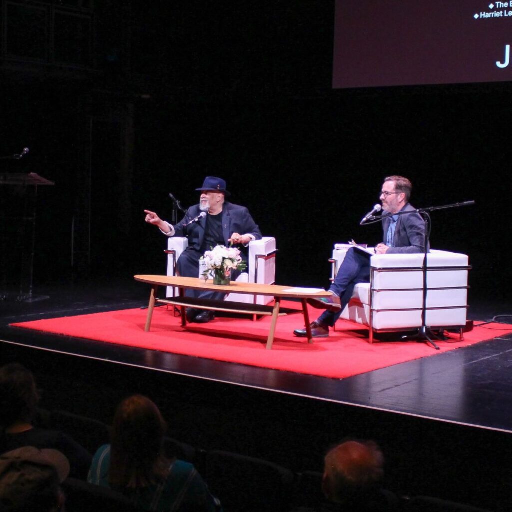 Walter Mosely on stage with Roland Gulliver during MOTIVE 2024. Walter is pointing out into the audience